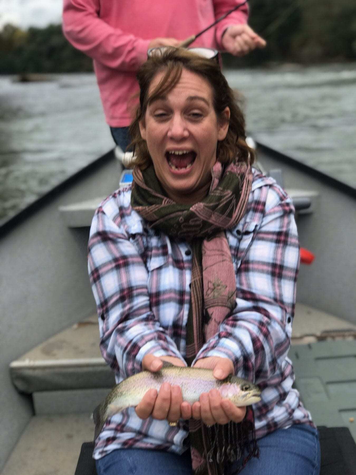 Travel blogger Kathy Brown and her husband Steve sitting in a samll fishing boat. Kathy has caught a fish and is holding it up for the camera with excitement. Her Husband looks in amazement in what she has caught before throwing back into the lake.