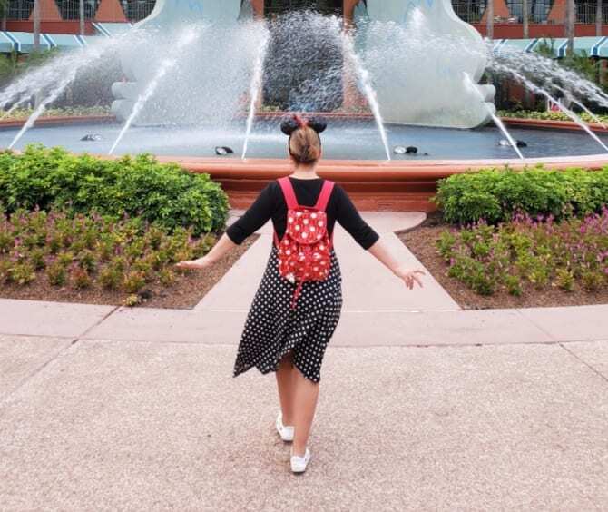 "Chattanooga travel blogger Kathy Brown, dressed in a stylish black and white polka dot dress, wearing vibrant red sequined Minnie Mouse ears and carrying a sequined backpack, strolls towards a magnificent Swan fountain at the Swan and Dolphin Resort in Orlando, Florida. With a sense of adventure in her stride, Kathy explores the enchanting surroundings, capturing the essence of Disney magic. The Swan fountain stands tall, its graceful beauty mirroring Kathy's excitement and joy during her visit. Join Kathy on her magical journey at the Swan and Dolphin Resort."