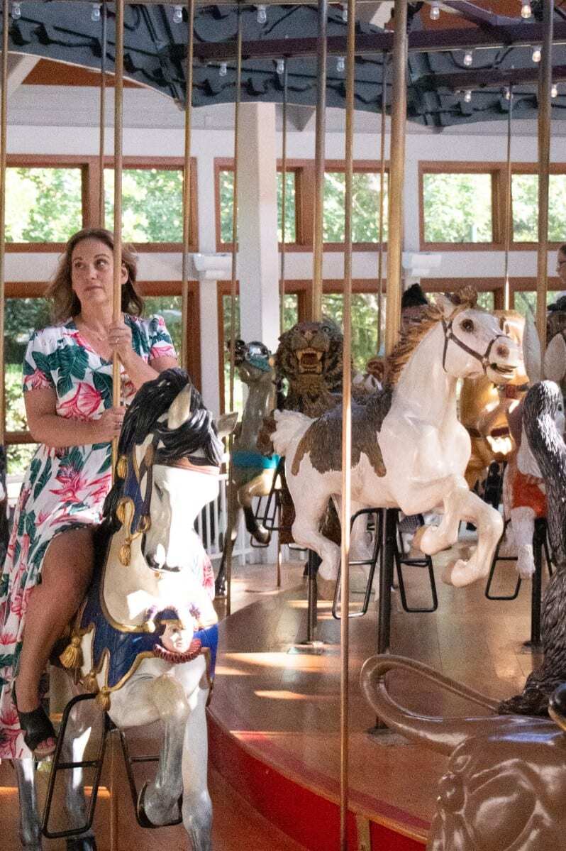Woman riding a merry go round carousel wearing a flower dress