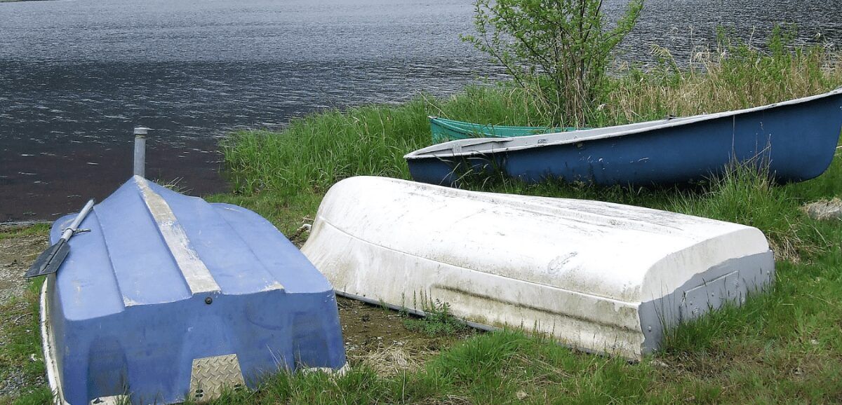 Blue and white canoes laying on a the banks of a lake. Image: Canva