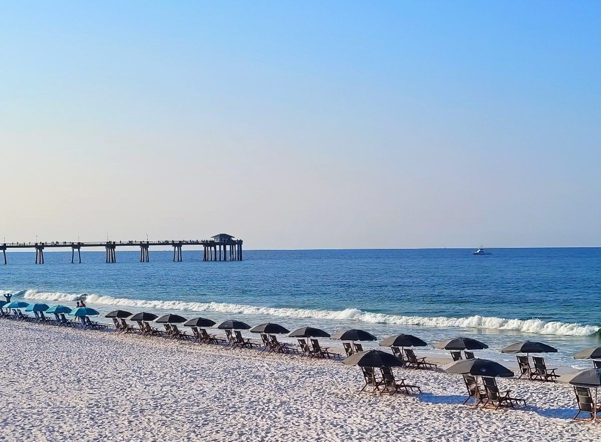 White sand beaches with beach umbrellas and lounge chairs. Pier in the background and emerald waters. Image: Kathy Brown Location: Fort Walton Beach Florida