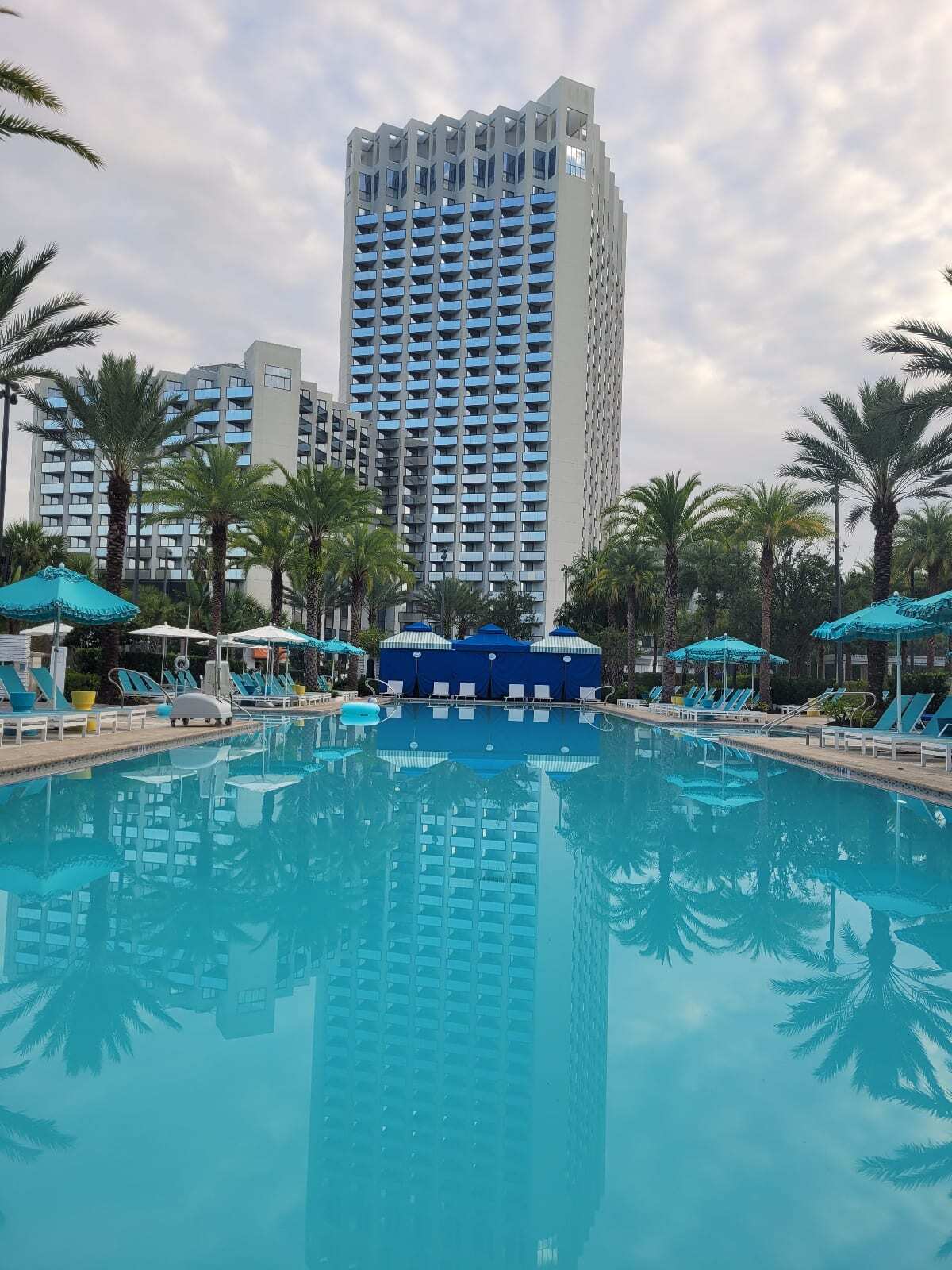 Large Outdoor pool surrounded by lounge chairs, umbrellas, cabanas, and facing a large resort building. Image: Kathy Brown Hilton Buena Vista Palace Resort Walt Disney World.