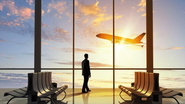 Man standing at a large window watching a plane take off.  Image: Canva 