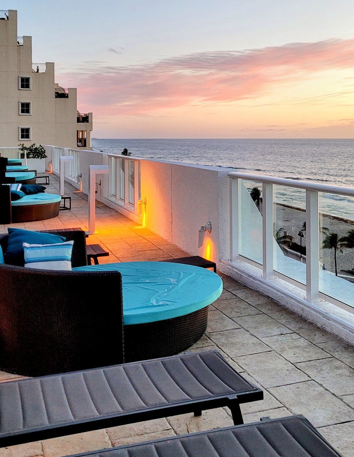 The pool deck of Conrad Hotel in Fort Lauderdale, Florida, offers a relaxing ambiance with circular daybeds lining the exterior glass partition. Guests can unwind and enjoy the picturesque view of the ocean and sandy beaches