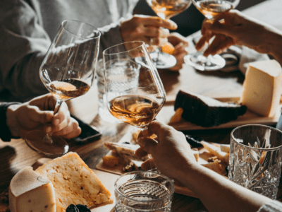 Glasses of wine being held by friends around a rustic table.