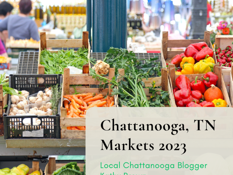 A vibrant farmers market in Chattanooga, Tennessee is depicted in this image. The foreground shows a colorful variety of freshly picked vegetables, including tomatoes, peppers, cucumbers, and carrots, displayed on tables and in wooden crates. In the background, a bustling crowd of people can be seen milling about, chatting with vendors and perusing the offerings. The atmosphere is lively and festive, with sunlight streaming in from overhead and tents providing shade for shoppers. Overall, the scene conveys a sense of community and celebration around locally grown produce.
