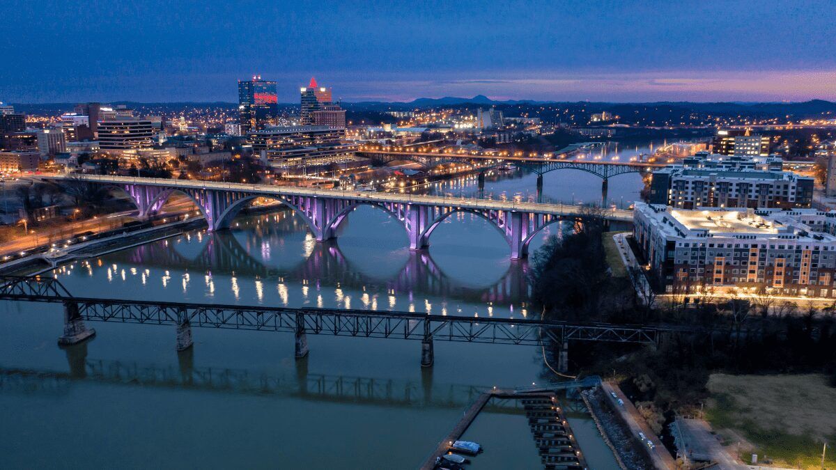"View of the Downtown Knoxville skyline with three bridges spanning across the Tennessee River, showcasing the city's vibrant urban landscape and natural water features."