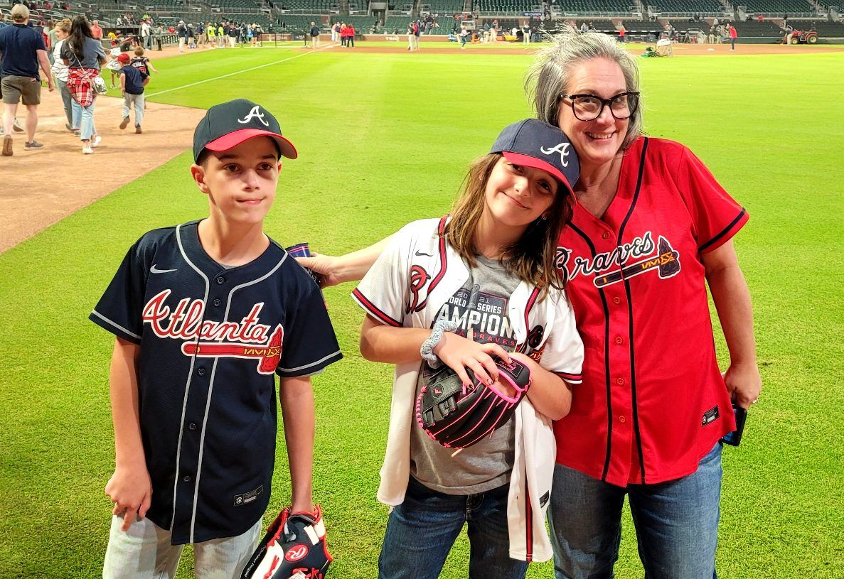 Travel Blogger Kathy Brown stands in the middle of Atlanta Braves baseball stadium with her two Grandchildren.