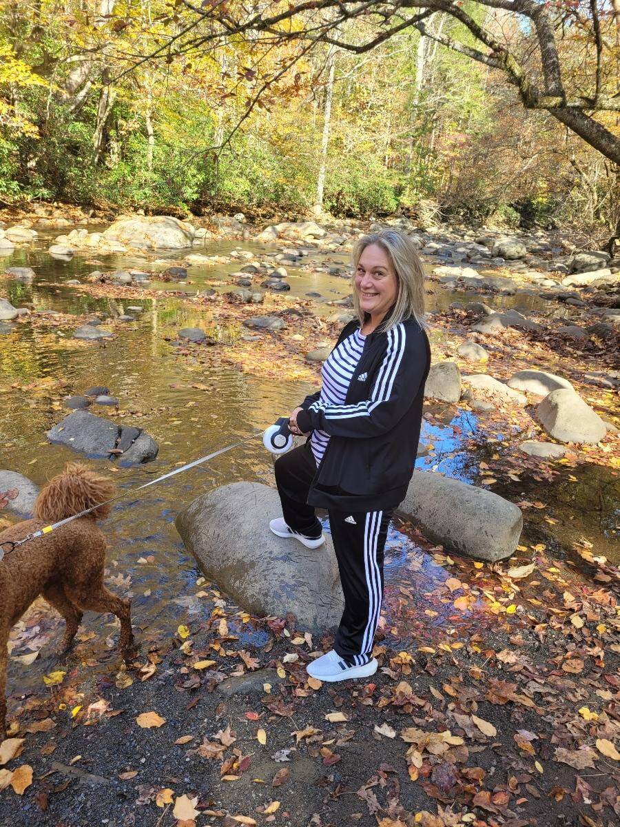 Travel blogger Kathy Brown walking her Goldendoodle puppy in the Smoky Mountains. Kathy is looking comfortable wearing an adidas tracksuit that is black with 3 white stripes down the arm and legs.