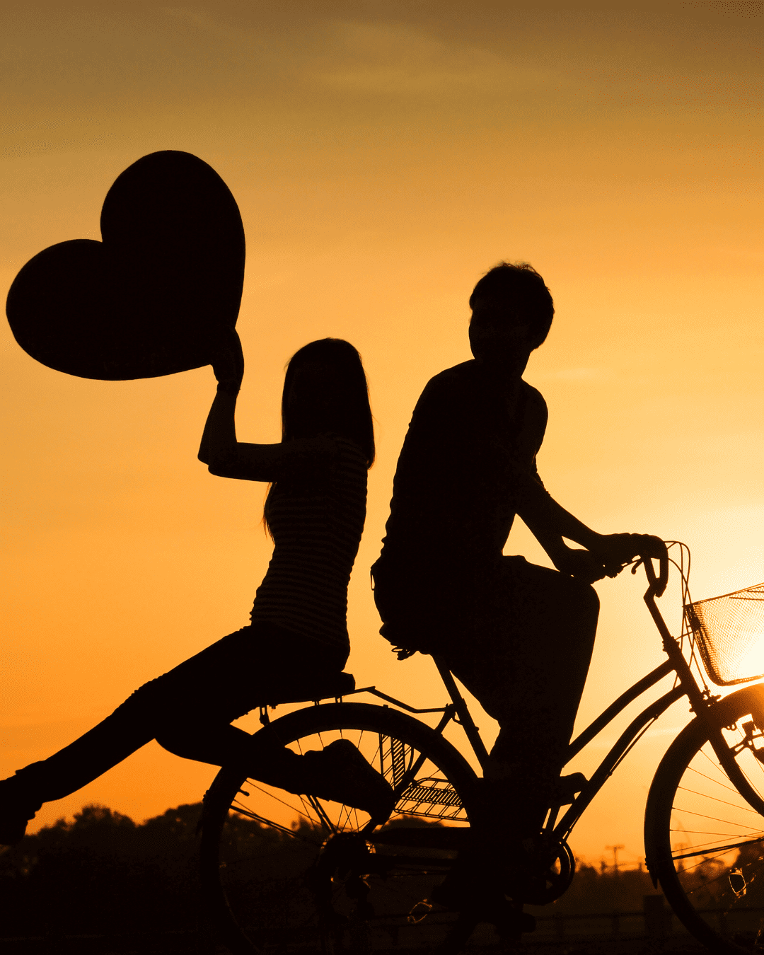 A blissful moment: A man and woman riding a tandem bike together against a breathtaking sunset backdrop, embracing the joy of shared adventures and love.