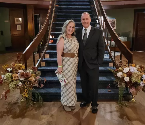 Local Chattanooga Tennessee blogger and travel writer Kathy Brown stands with her husband at the foot of an elegant staircase at the Hotel Chalet Grand opening. Both are dressed and looking ready for a glamorous evening out.